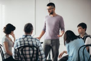 Young sad man talking to the group of people during psychotherapy