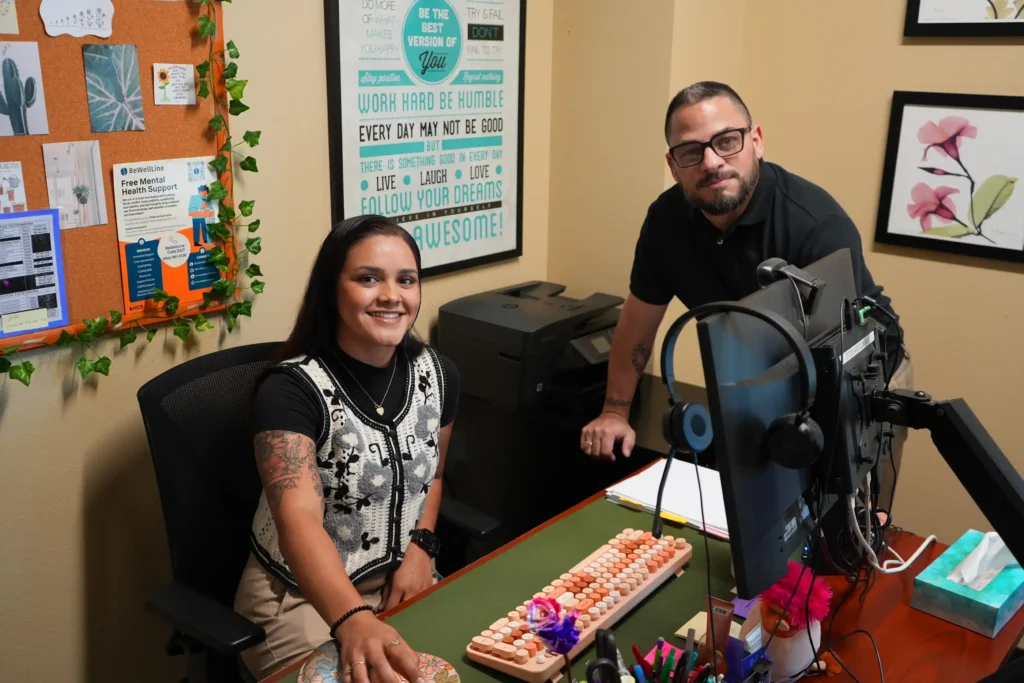 Person sitting at a desk with another person standing next to the desk