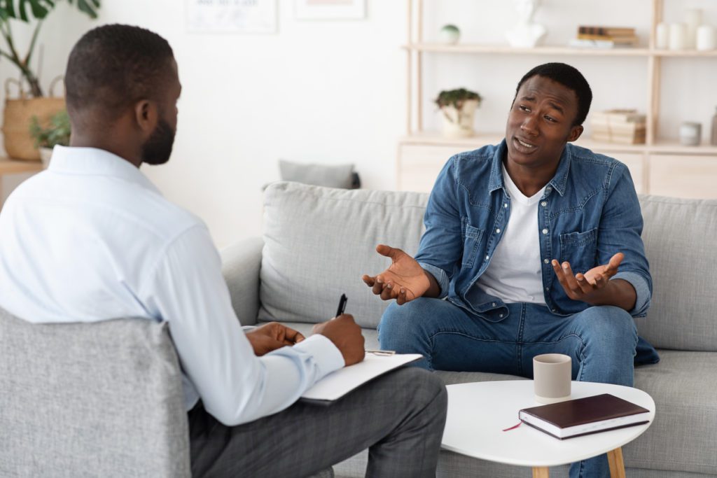 Stressed black man explaining his problems to psychologist at individual therapy session